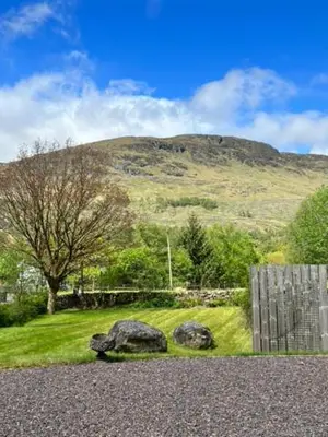 a field with two rocks and a hill in the background at Beautiful Farm House at the foot of Ben More. in Crianlarich