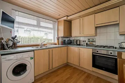 a kitchen with wooden cabinets and a washer and dryer at Centrally Situated 1 Bedroom House in Cumbernauld in Cumbernauld