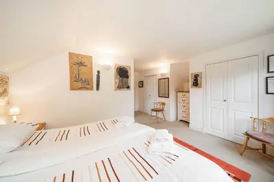 a white bedroom with two beds and a chair at Earnside Cottage in Comrie