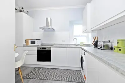 a white kitchen with white cabinets and a black dishwasher at JOIVY Modern Flat on Rose Street in Edinburgh