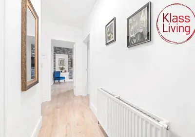 a white hallway with paintings on the wall and a mirror at Sanderson Apartment by Klass Living Uddingston in Uddingston