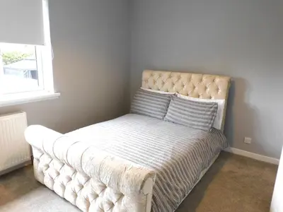 a tufted bed in a bedroom with a window at Beautiful 3 bedroom home with large garden 35 mins to Glasgow & Edinburgh in Whitburn