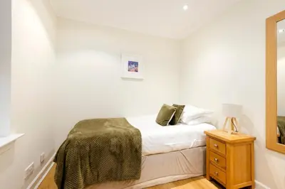 a white bedroom with a bed and a night stand at JOIVY Lovely Flats near the City Centre in Edinburgh
