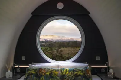 a round window in a bedroom with a view of a mountain at Endrick Escape - Luxury Glamping in Gartness