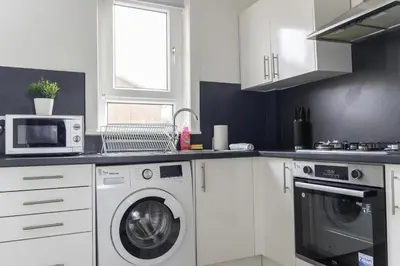 a white kitchen with a washing machine and a microwave at Raploch House in Larkhall