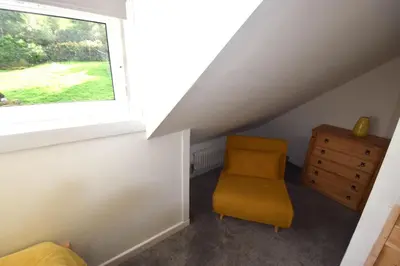 an attic room with a chair and a window at 1 Planetree Cottage - Loch View in Lochgoilhead