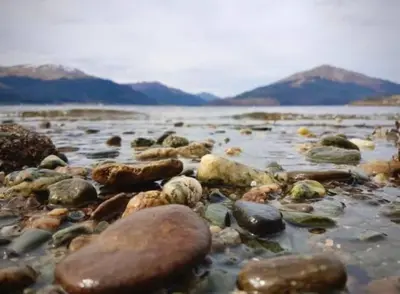 a group of rocks on a beach with mountains at Superb Loch Side Apartment with Sea & Sunset Views in Helensburgh
