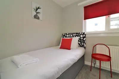 a small bedroom with a bed and a red chair at Signature - Sydney House in East Kilbride