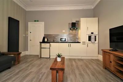 a kitchen with white cabinets and a table in a living room at Signature - Linden House Flat 4 in Airdrie