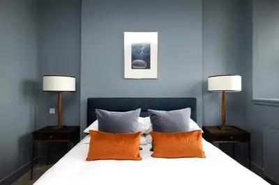 a blue bedroom with a bed with orange pillows at JOIVY Stylish Flat in New Town in Edinburgh