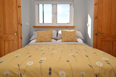 a bed with a yellow comforter and a window at Bay View in Lochgilphead