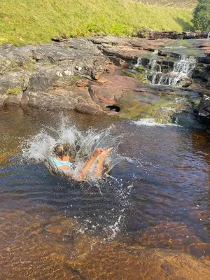 a person swimming in the water near a waterfall at Exclusive private estate cottage in Lochearnhead