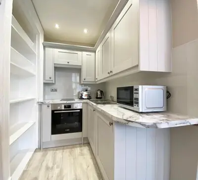 a white kitchen with white cabinets and a microwave at The Buckingham Studio in Glasgow