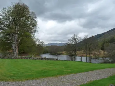 a grassy field with a lake in the background at Riverside Cottage, Bridge of Balgie, Glenlyon, Perthshire in Bridge of Balgie