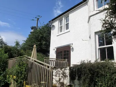 a white house with a wooden fence and an umbrella at Cologin Farmhouse in Oban