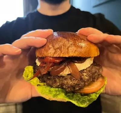 a man holding a large hamburger with his hands at The Rhu Inn in Rhu