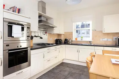 a kitchen with white cabinets and a wooden table at JOIVY Modern Flat with Free Parking in Edinburgh
