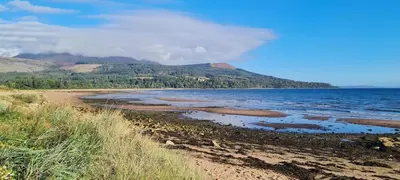 a beach with the ocean and mountains in the background at 3 bedroom cosy cottage in Lamlash, Isle Of Arran in Lamlash