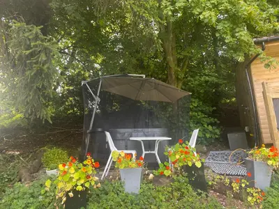 a patio with a table and an umbrella and flowers at Unique Orchard Lodge for couples with hot tub in Strathaven
