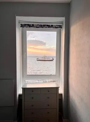 a window with a dresser and a ship in the ocean at Anchorage, a lovely 2nd floor one bedroom apartment with fabulous seaviews in Largs