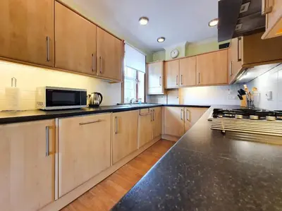 a kitchen with wooden cabinets and a black counter top at Parkgate Apartment - Near M90, Amazon, Edinburgh in Rosyth