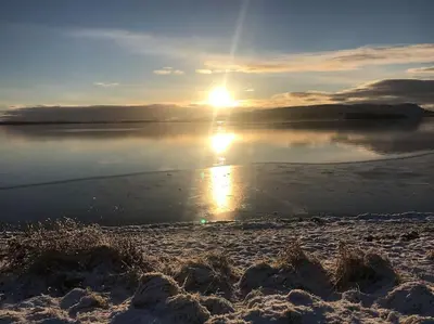 a sunset on a beach with the sun reflecting in the water at Loch Leven Getaway - 2 bed house in Kinross