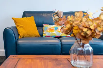 a blue couch with yellow pillows and a vase on a table at Lovely 3-bedroom flat with free parking in Bridge of Allan