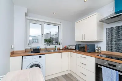 a kitchen with white cabinets and a washer and dryer at Lovely 3-bedroom flat with free parking in Bridge of Allan