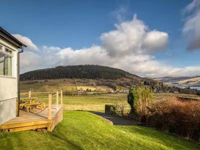 a wooden deck with a picnic table in a field at Ciaran Cottage in Stron-fearnan