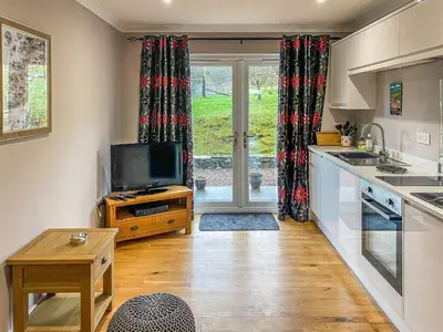 a kitchen with a tv and a table and a kitchen with curtains at Dalnafeidh Beag - Cottage in Portnacroish