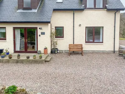 a bench in front of a house with potted plants at Dalnafeidh Beag - Cottage in Portnacroish