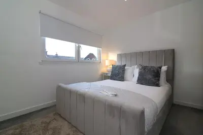 a white bedroom with a large bed with a window at Glas Go Executive 2-Bedroom Apartment near OVO Hydro Free Parking in Glasgow