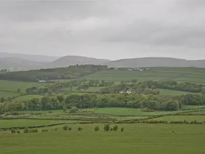 a green field with trees and hills in the background at The Coach House at Stewart Hall in Rothesay