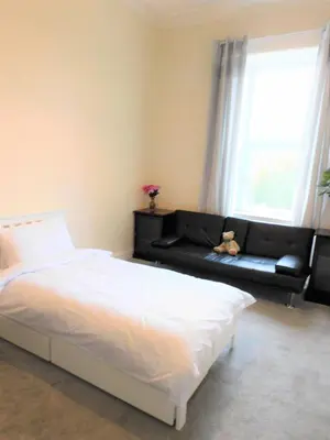 a bedroom with a bed and a black couch at Comfortable 4 bed Apt in Paisley Next to Station in Paisley