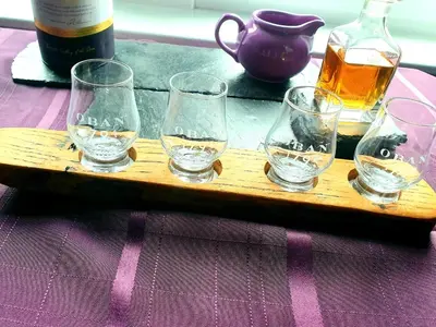 a wooden tray with four glasses and a bottle of whiskey at The Distillers Den in Oban