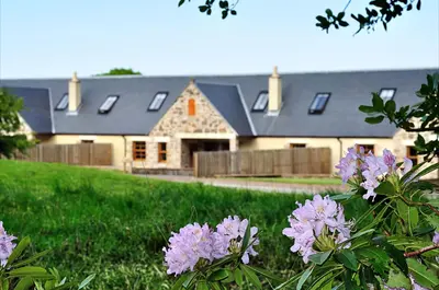 a house with a yard with purple flowers in front of it at Rose Cottage at Williamscraig Holiday Cottages in Linlithgow
