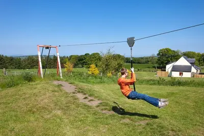 a woman is swinging on a zip line at Beech Cottage at Williamscraig Holiday Cottages in Linlithgow