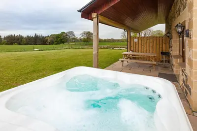 a jacuzzi tub in a yard with a bench at 1 Eden at Williamscraig Holiday Cottages in Linlithgow