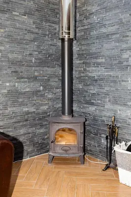 a wood stove in a room with a brick wall at 1 Eden at Williamscraig Holiday Cottages in Linlithgow