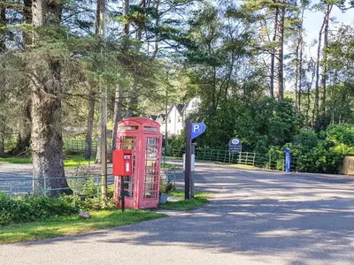 an old red phone booth on the side of a road at Lochside Apartment in Stronachlachar