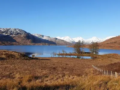 a lake with trees and mountains in the background at Lochside Apartment in Stronachlachar