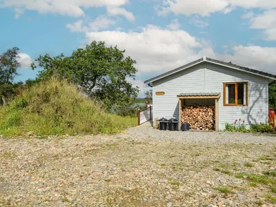 a small white building with a pile of fire wood at Teasel Lodge - Uk39647 in Lunga