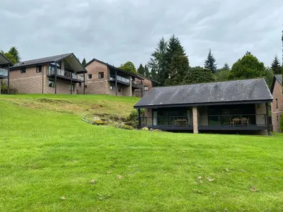 a house on a hill with a green field at Fabulous Lodges at Cameron House, Loch Lomond in Balloch