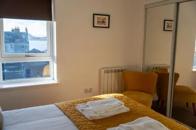 a bedroom with a bed and a chair and a window at Ledaig Apartment in Oban