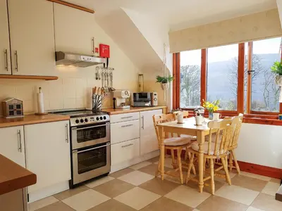 a kitchen with white cabinets and a table with chairs at The Old Post Office On Loch Tay in Stron-fearnan