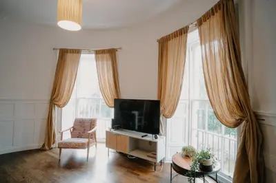 a living room with a tv and a chair and windows at Slateford House 1770 Luxury Aparthotel by The House of Danu in Edinburgh