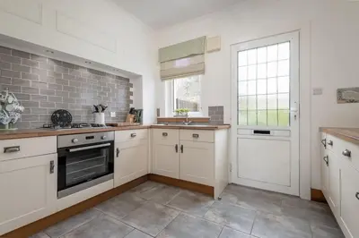 a large kitchen with white cabinets and a window at Heather Cottage, 2 bedroom in Comrie in Comrie
