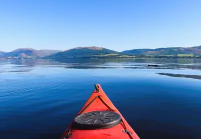 a red kayak on a lake with mountains in the background at An Cuilidh in Port Bannatyne