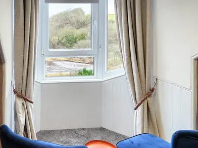 a living room with two windows and a blue chair at Riverside Cottage in Larkhall