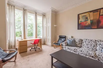 a living room with a couch and a desk and windows at Beautiful 2 Bed 2 Bath Flat overlooking Meadows Park in Edinburgh